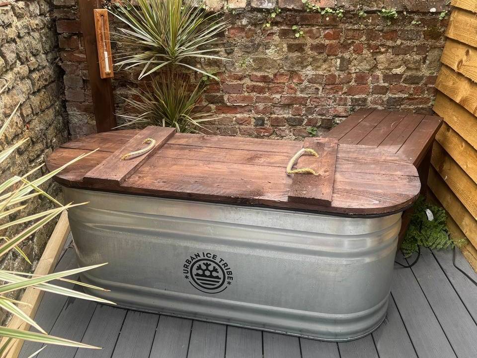 Ice bath cold plunge tub in outdoor courtyard with brick wall and plants