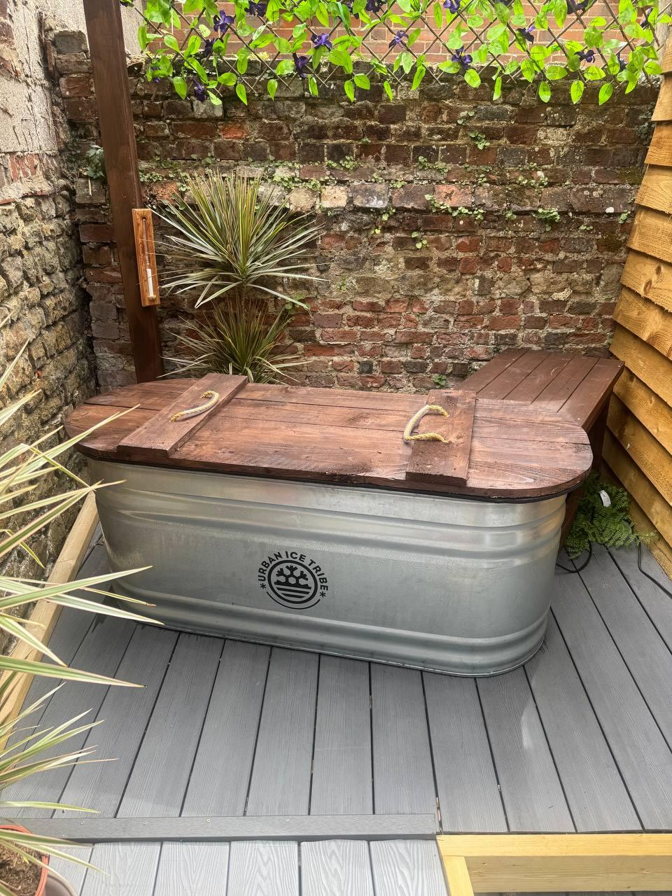 Ice bath cold plunge tub in outdoor courtyard with brick wall and plants